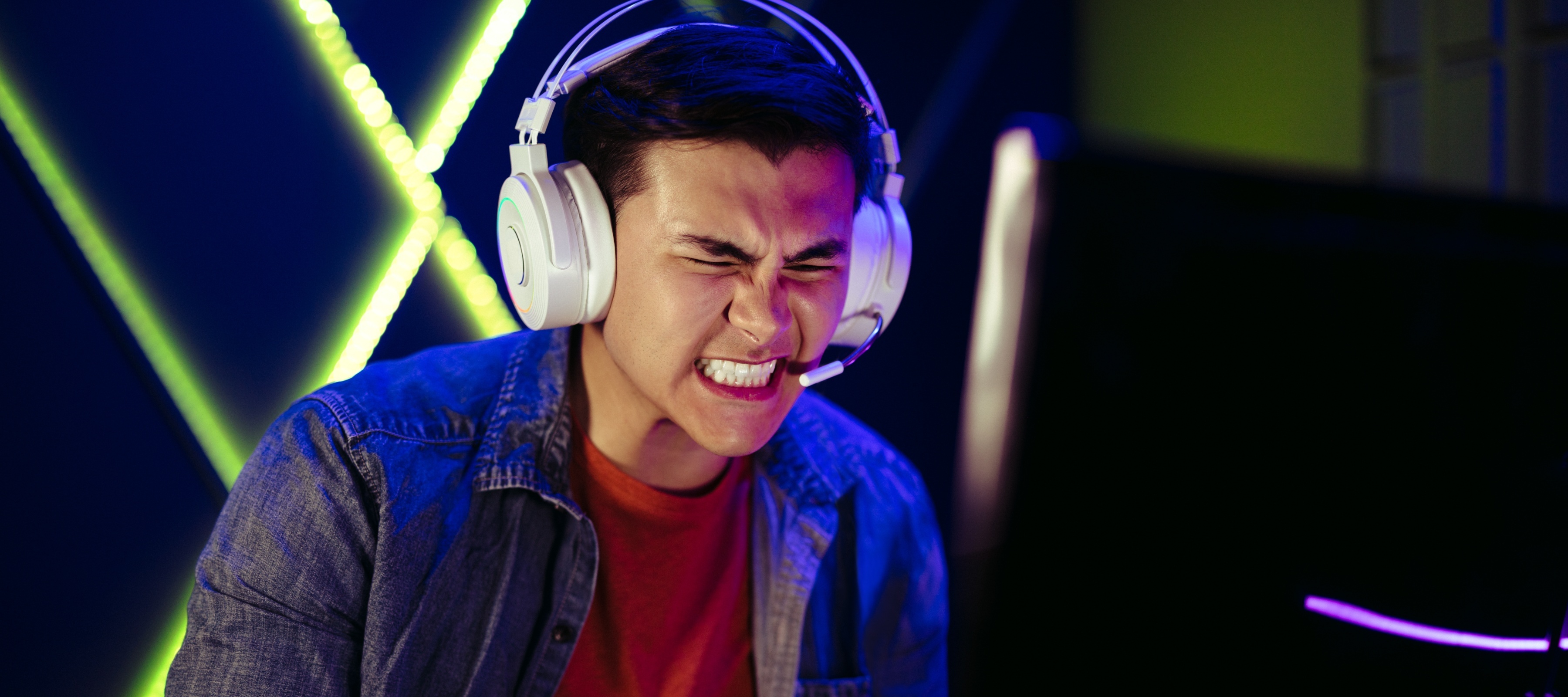 A man cringes while playing a game in front of a giant X logo