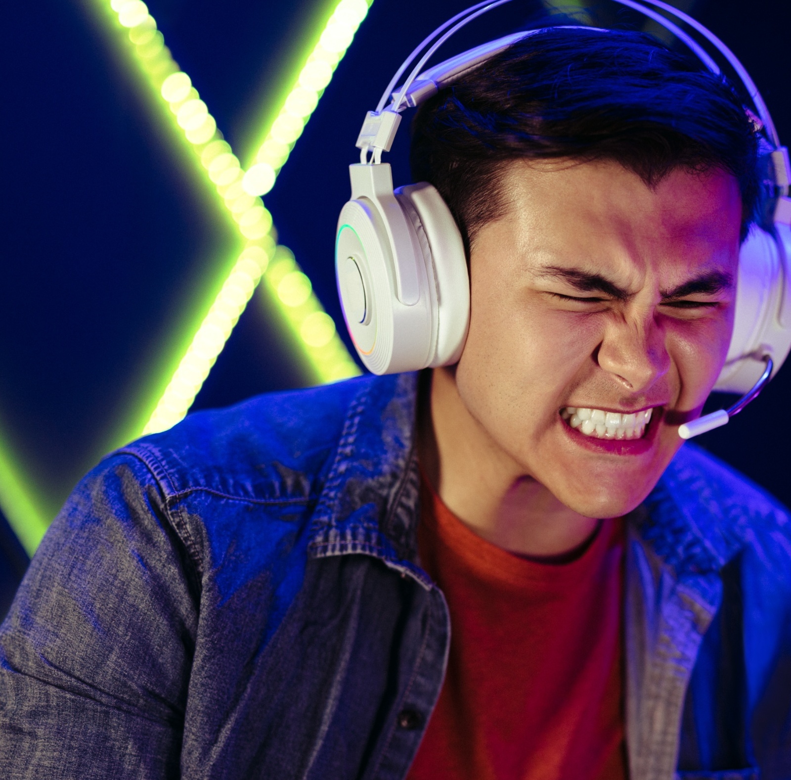 A man cringes while playing a game in front of a giant X logo