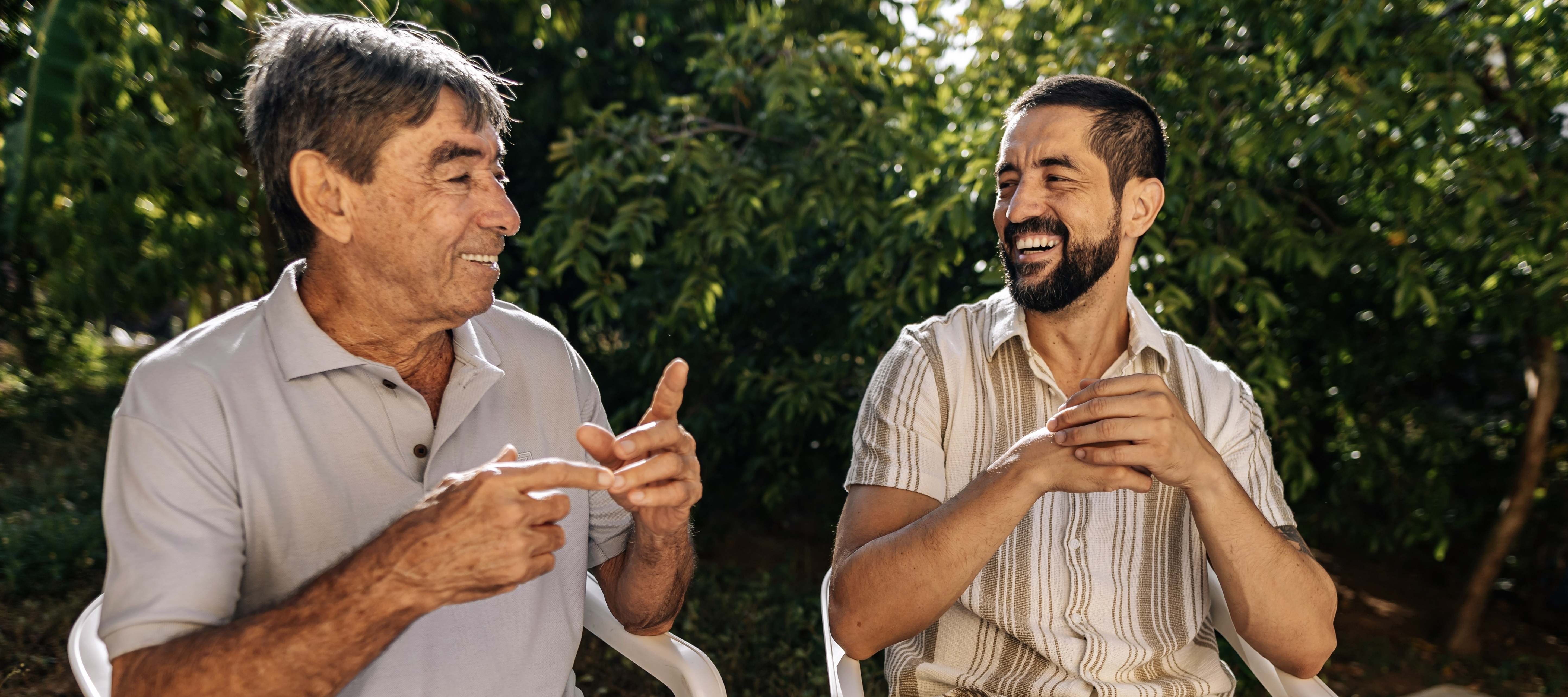 A senior father and adult son sit outside enjoying the outdoors.