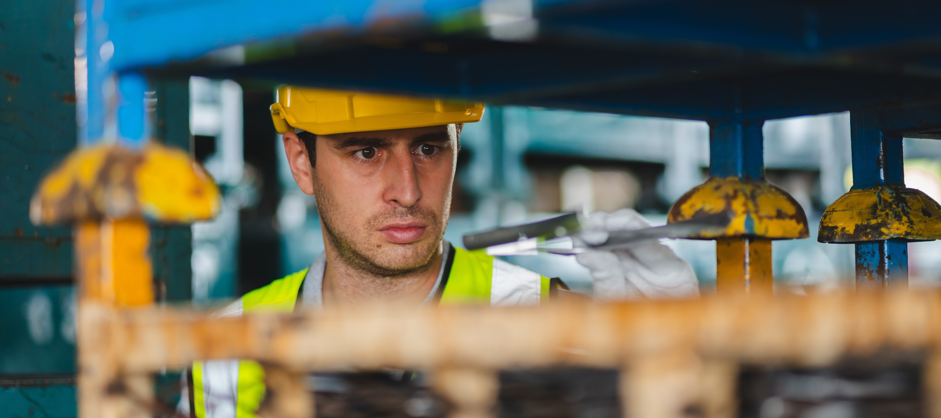 Man with serious look on his face, working in hard hat and reflective vest on industrial machine.