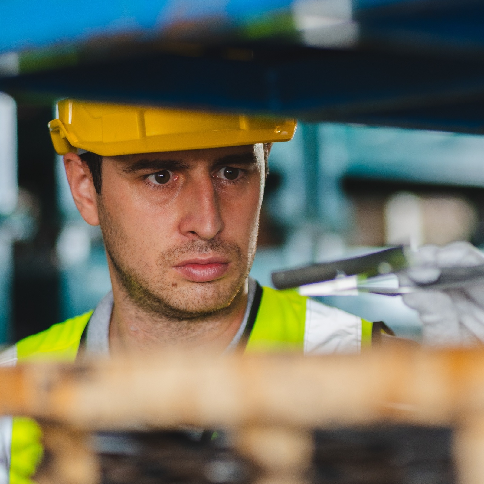 Man with serious look on his face, working in hard hat and reflective vest on industrial machine.