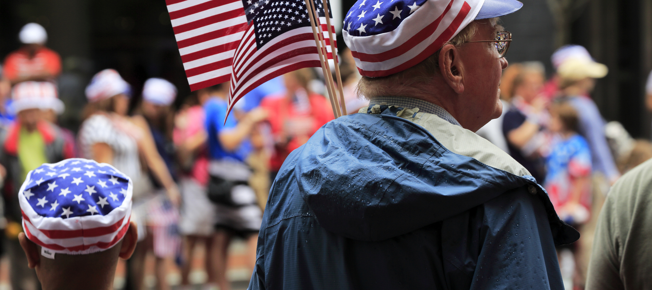 People in star and stripes hat carry US flag watching Independence Day parade.