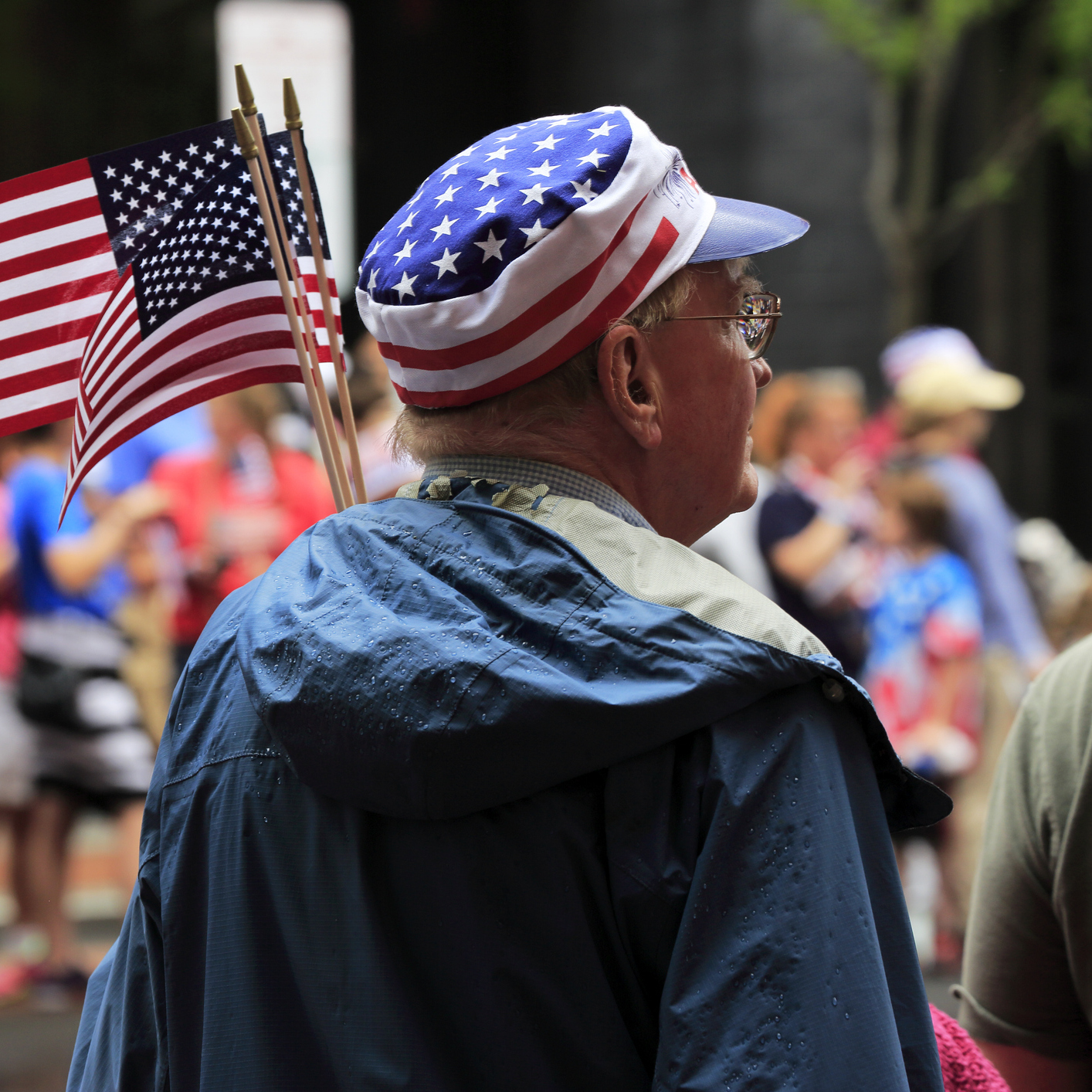 People in star and stripes hat carry US flag watching Independence Day parade.