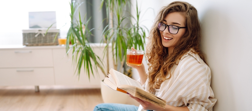 Young woman sitting on floor, drinking tea and reading book.