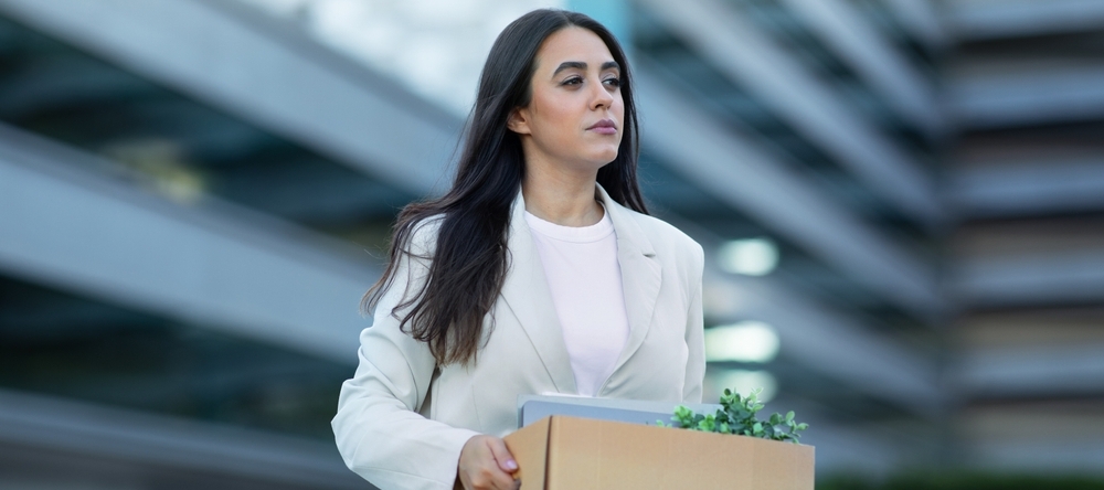 A photo of a businesswoman carrying a box of her desk supplies