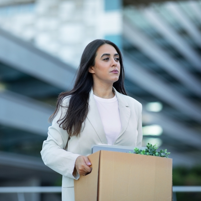 A photo of a businesswoman carrying a box of her desk supplies