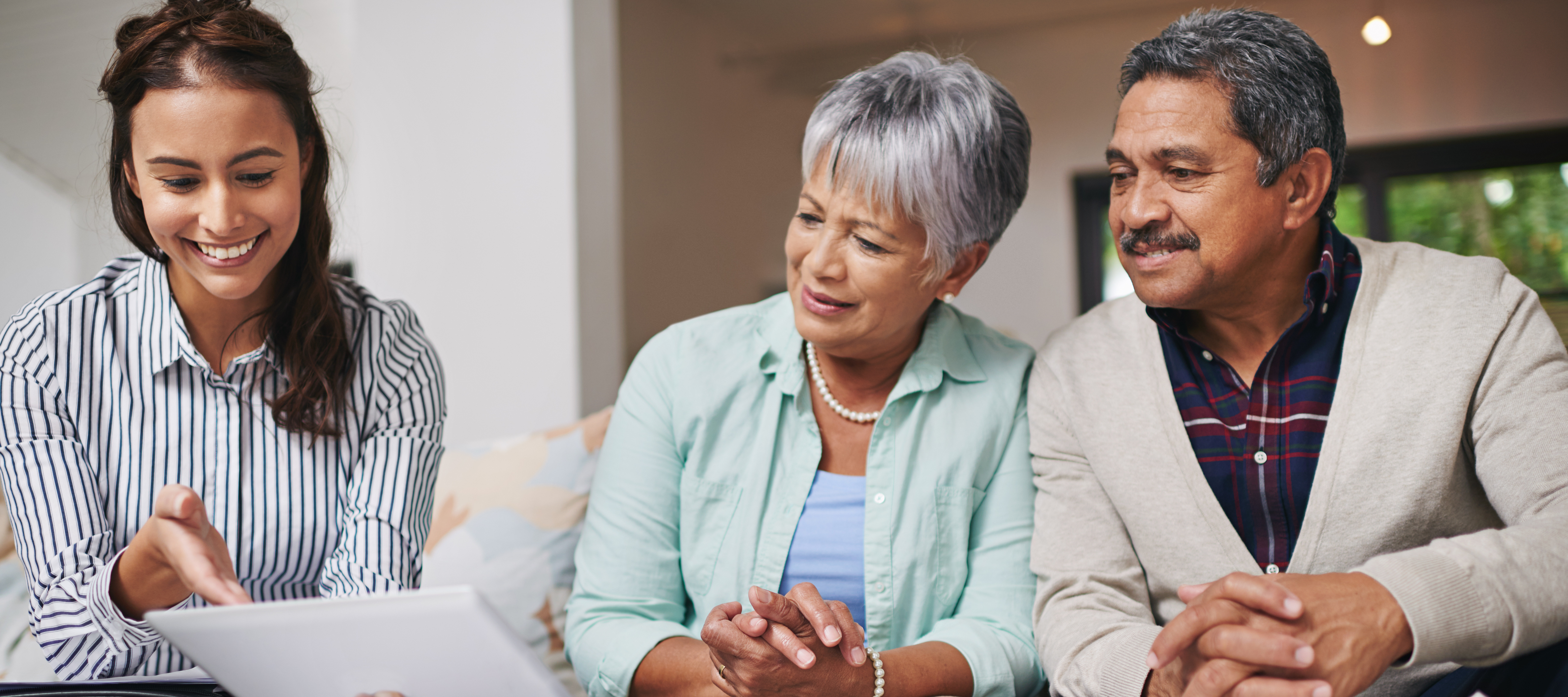 A financial advisor sits with a retired couple on a couch reviewing documents, smiling.