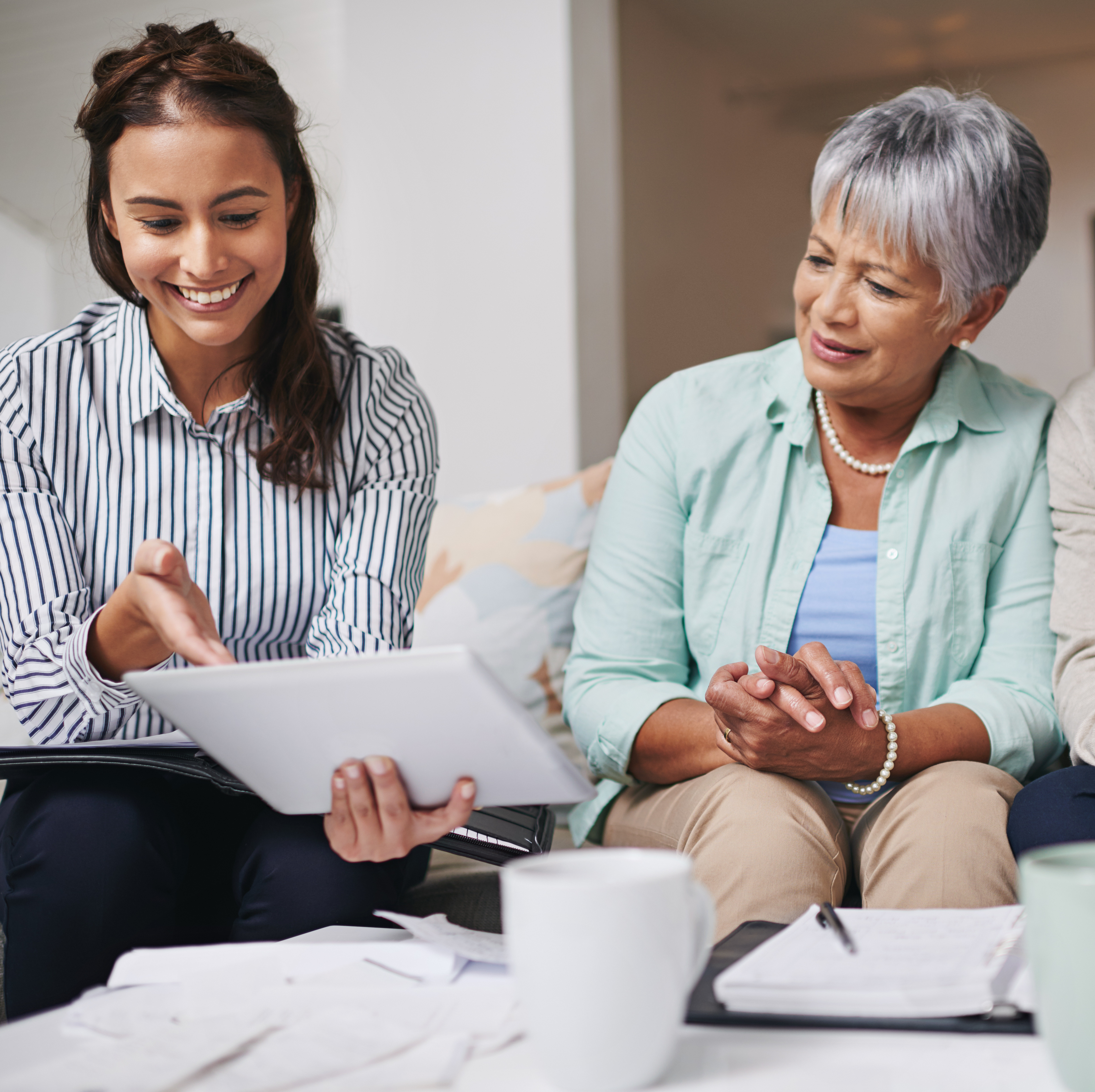 A financial advisor sits with a retired couple on a couch reviewing documents, smiling.