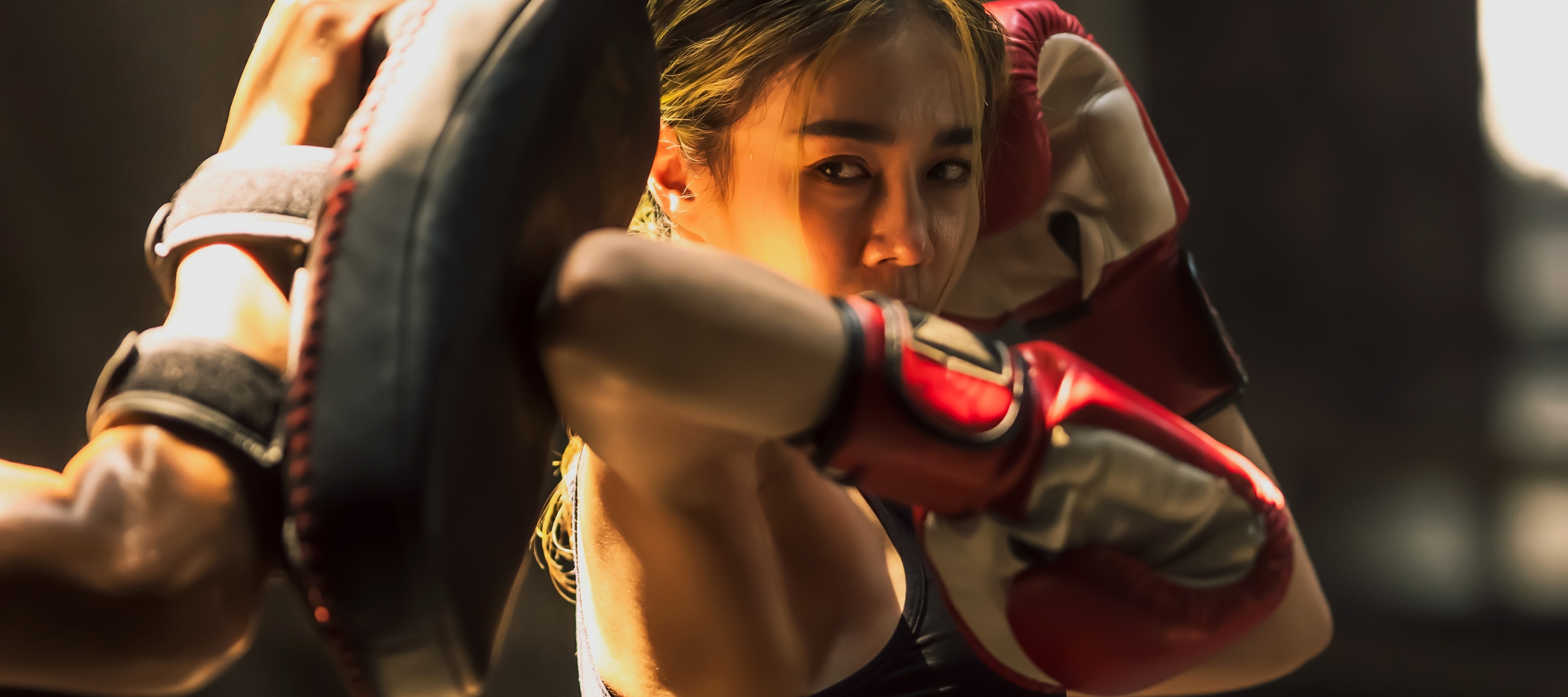 Portrait young Muay Thai boxer woman practicing boxing with elbow and boxing pad in gym.