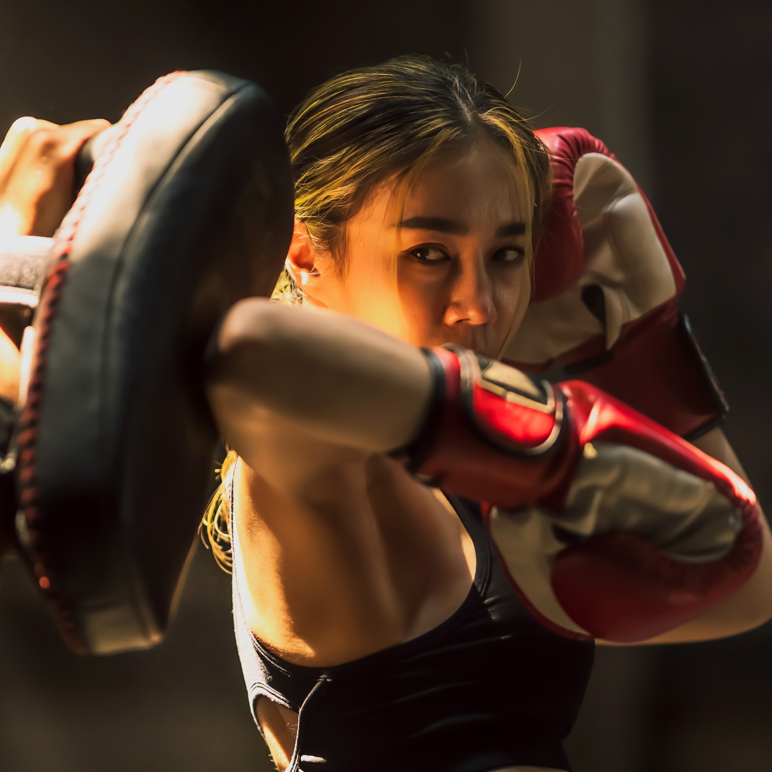 Portrait young Muay Thai boxer woman practicing boxing with elbow and boxing pad in gym.