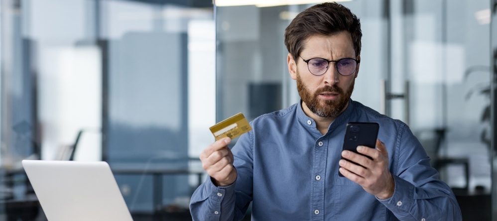 Confused man looking at his phone while holding a credit card.