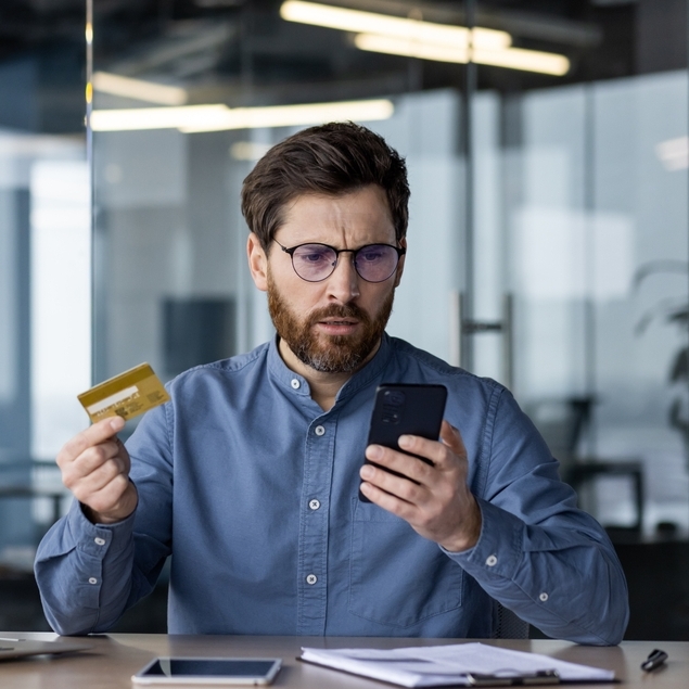 Confused man looking at his phone while holding a credit card.