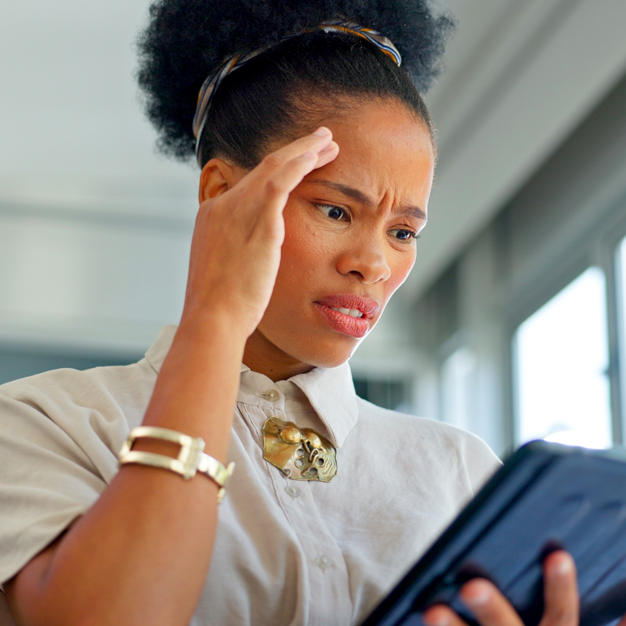 A young woman holds two fingers to her temple in frustration as she looks at a tablet.