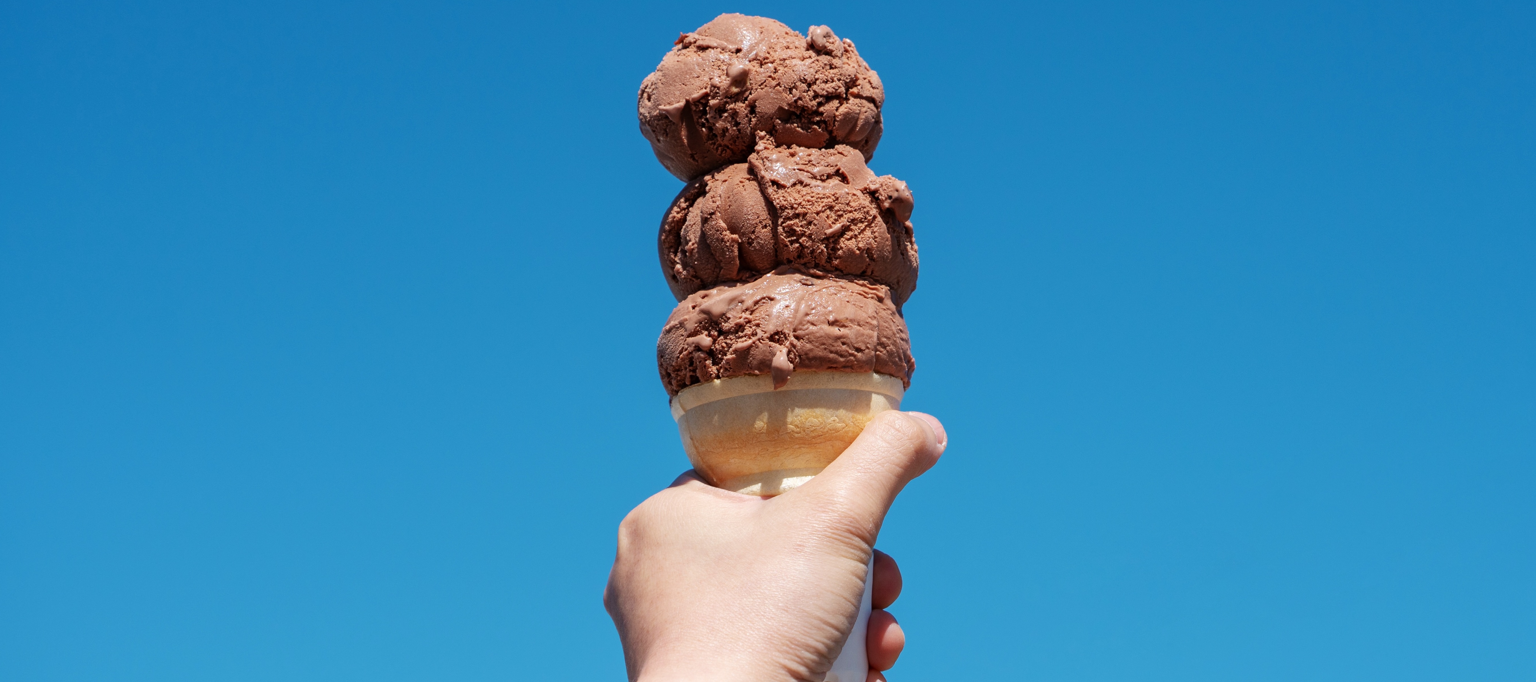 Hand holding chocolate ice cream cone to the sky