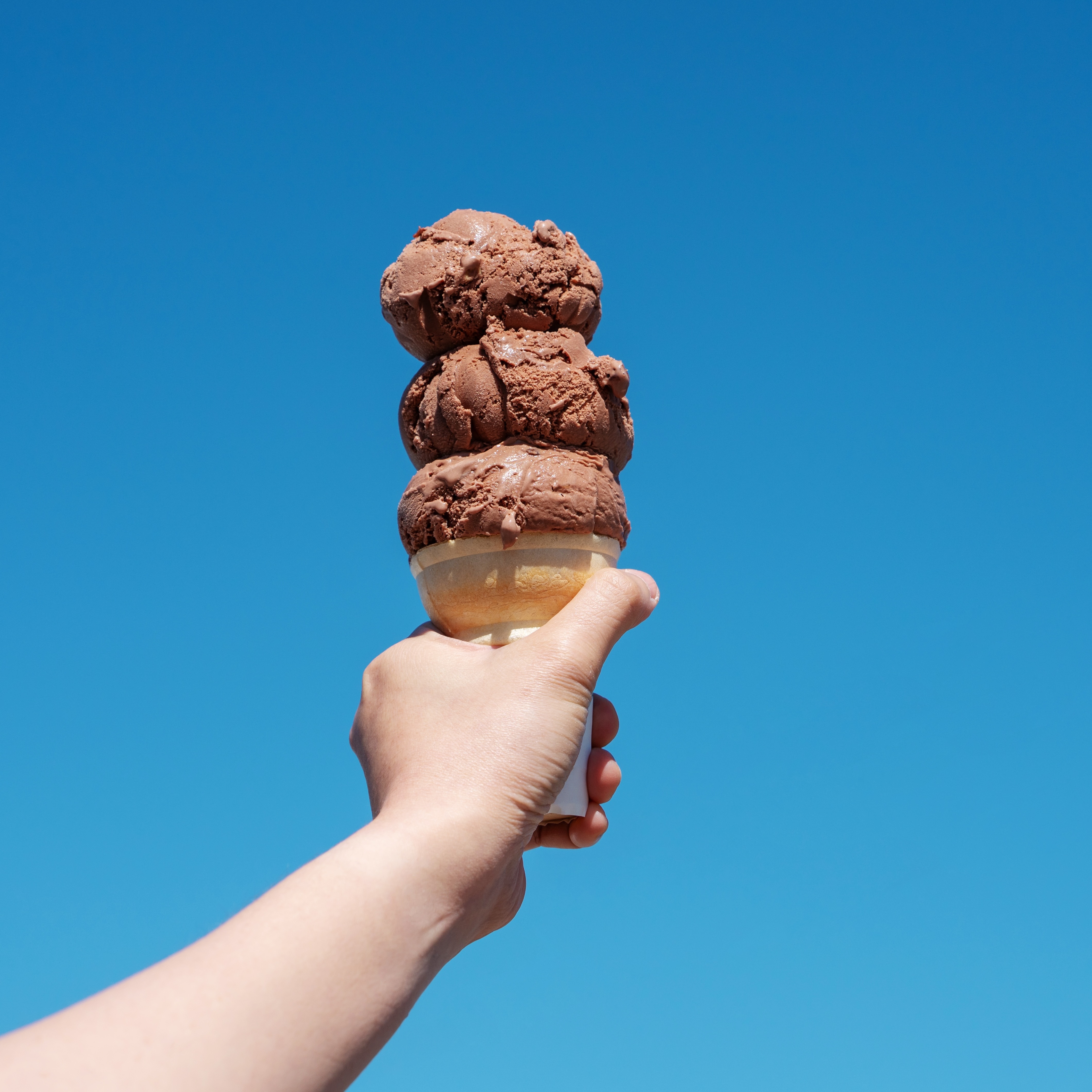 Hand holding chocolate ice cream cone to the sky