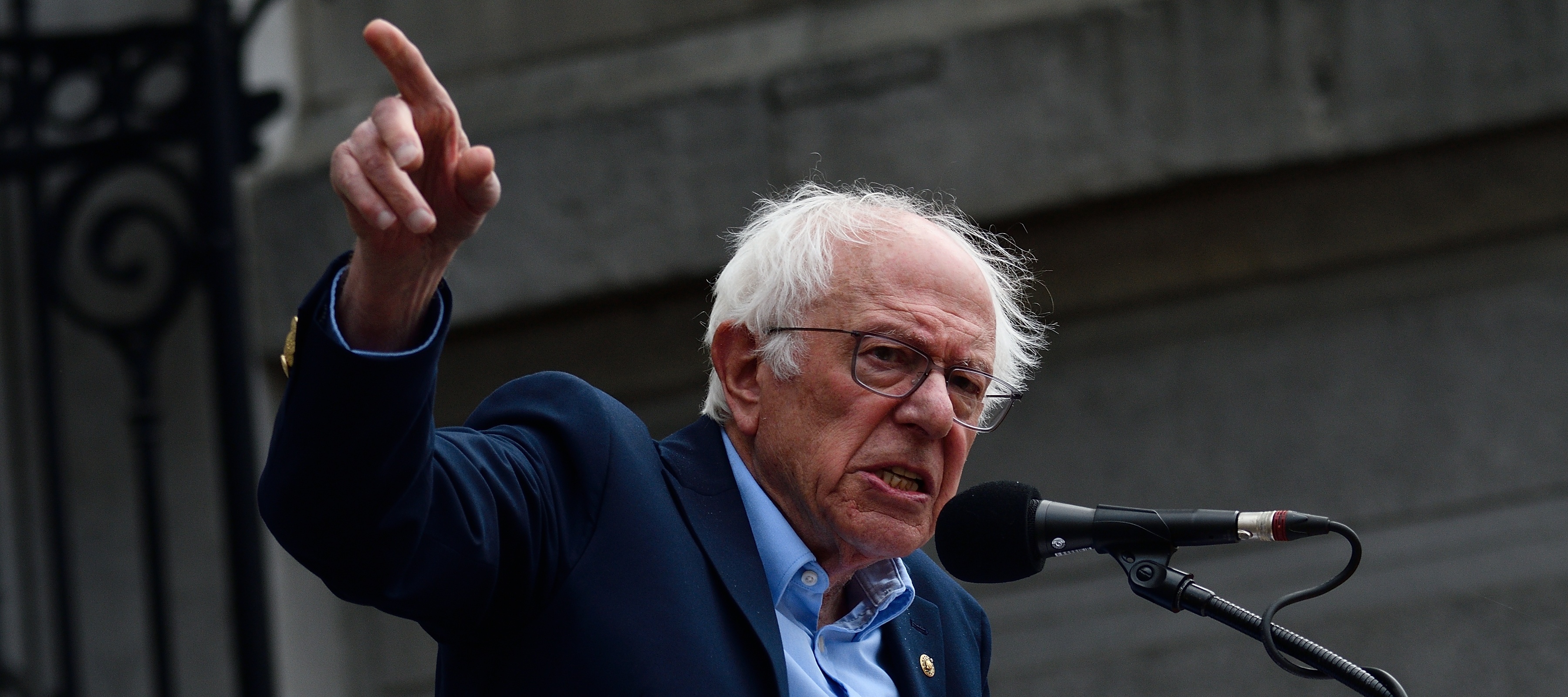 Bernie Sanders speaks into a microphone angrily pointing his finger to the sky