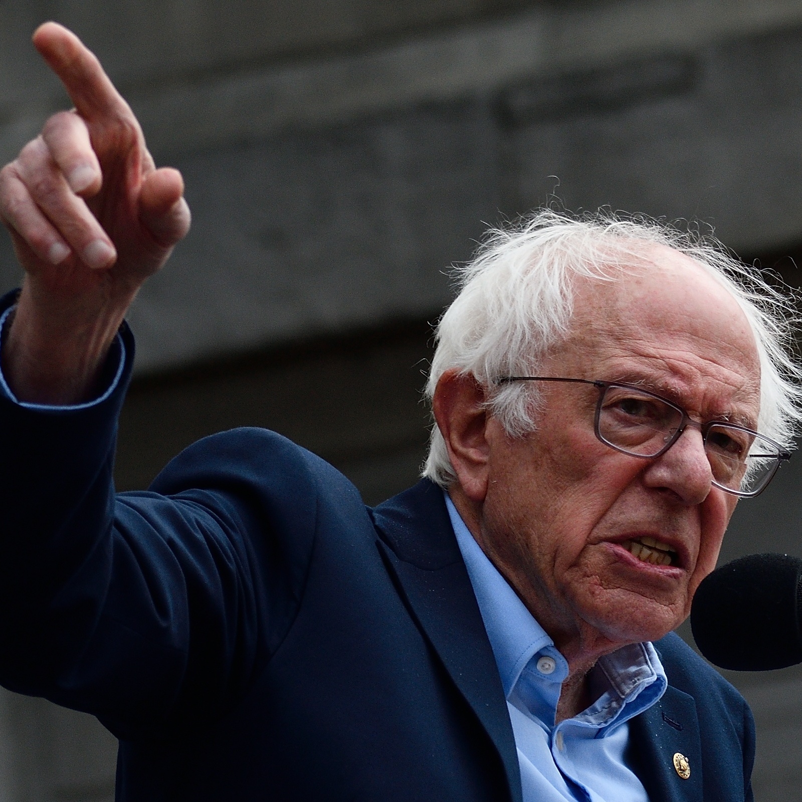 Bernie Sanders speaks into a microphone angrily pointing his finger to the sky