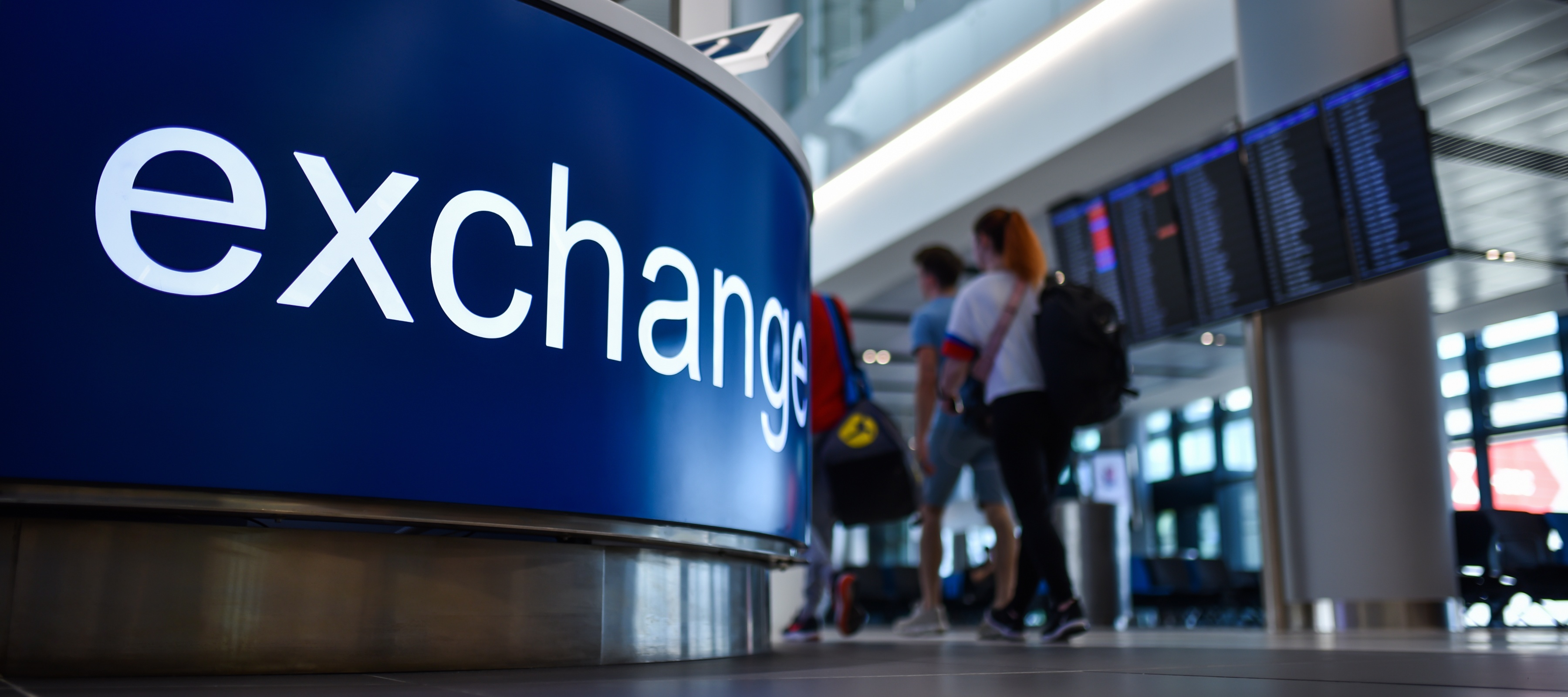 People walking by a currency exchange sign at the airport.