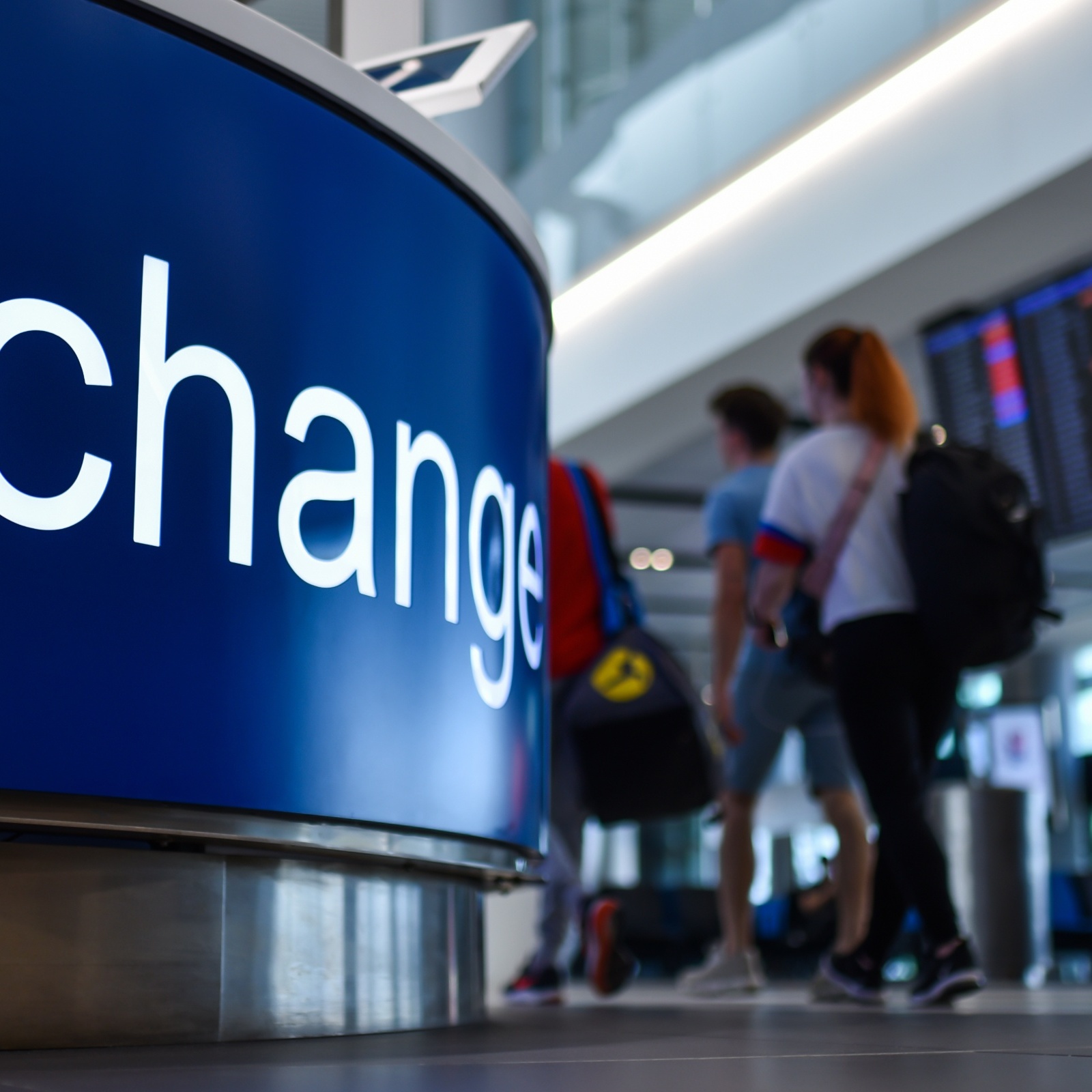 People walking by a currency exchange sign at the airport.