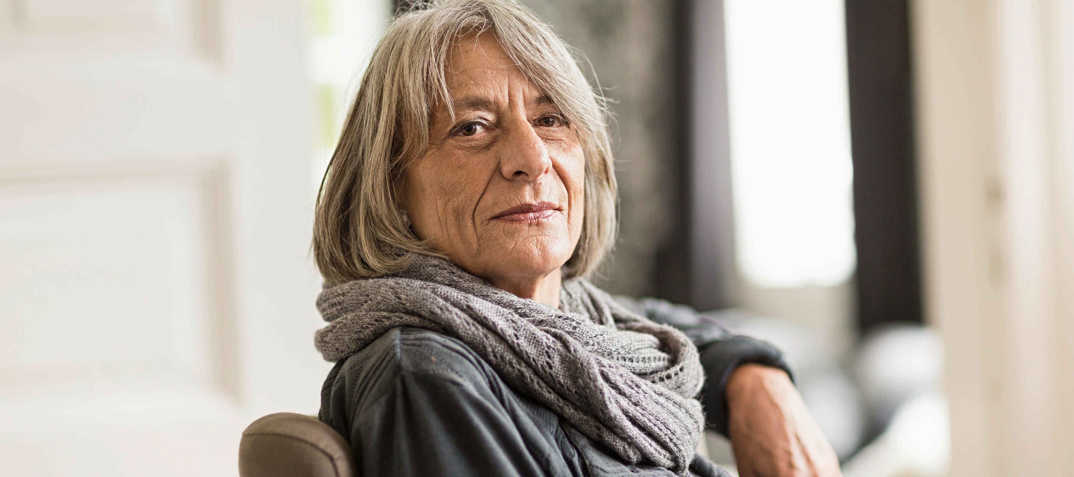 Older woman sitting in a chair, looking directly at the camera with a neutral, interested face.