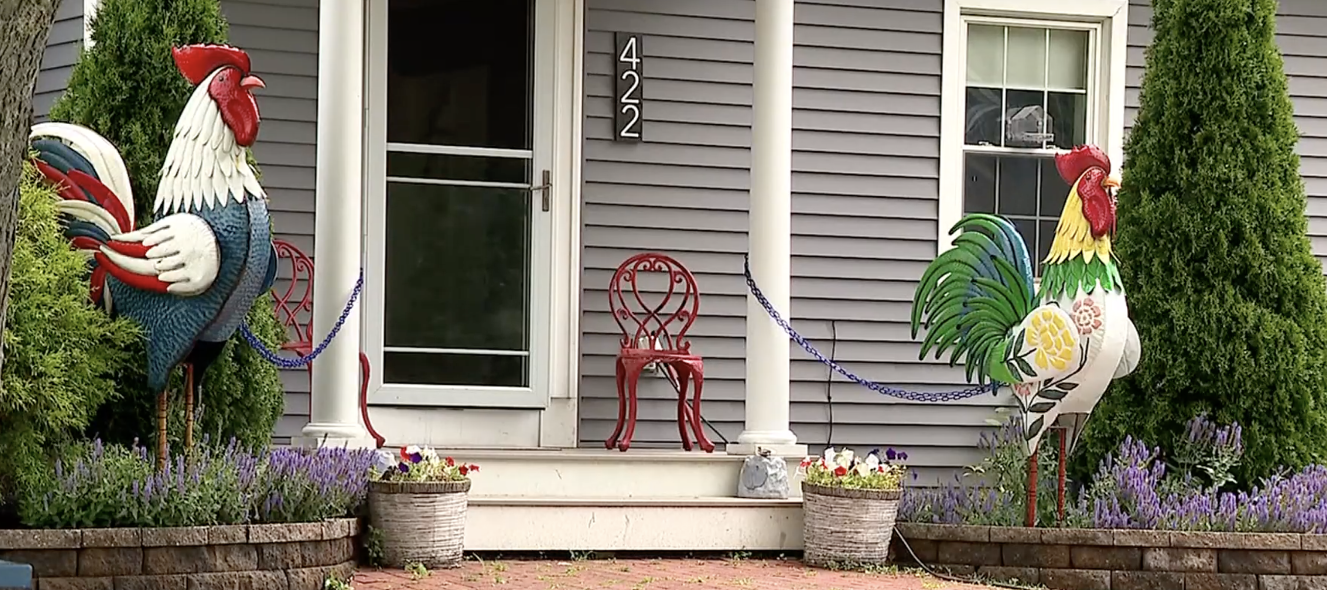 A photo of two rooster statues outside of a house