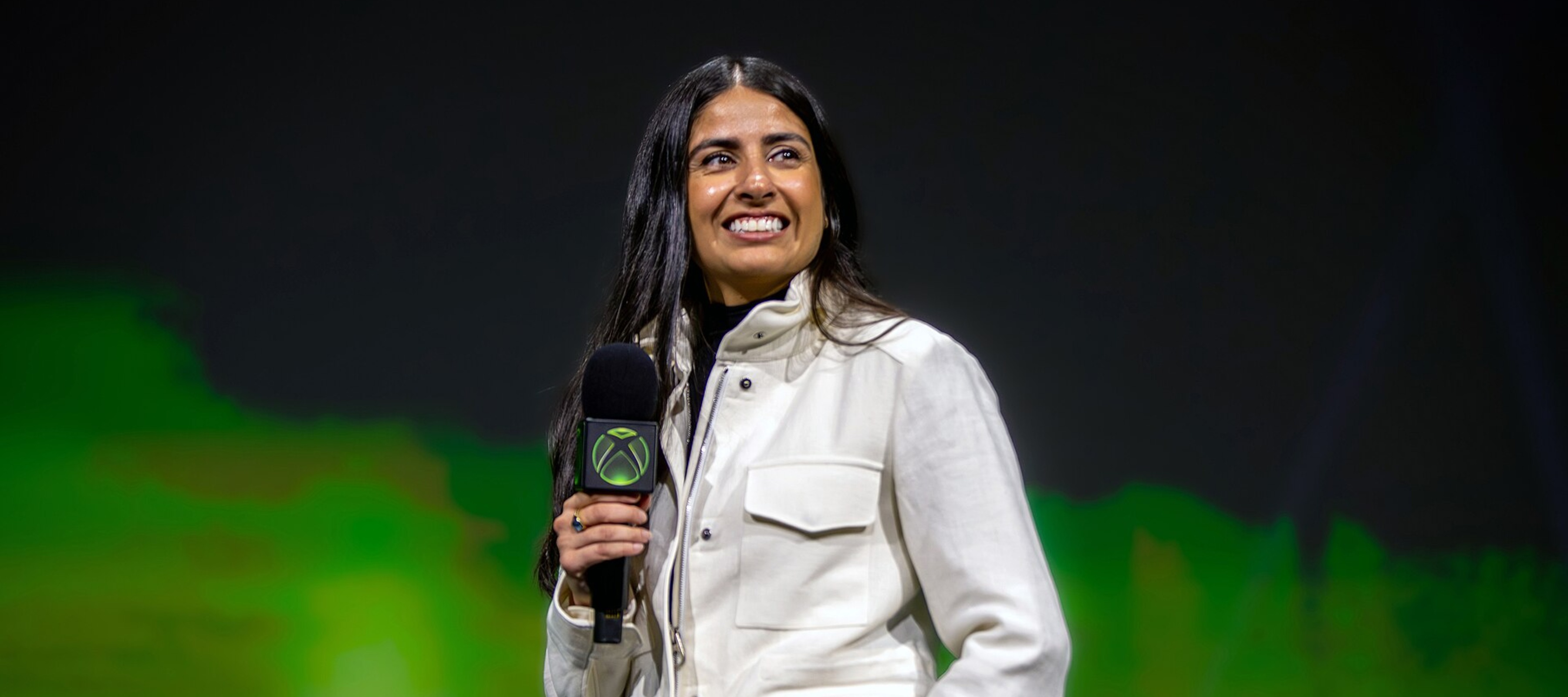 Xbox CEO Asha Sharma smiling on stage holding a microphone