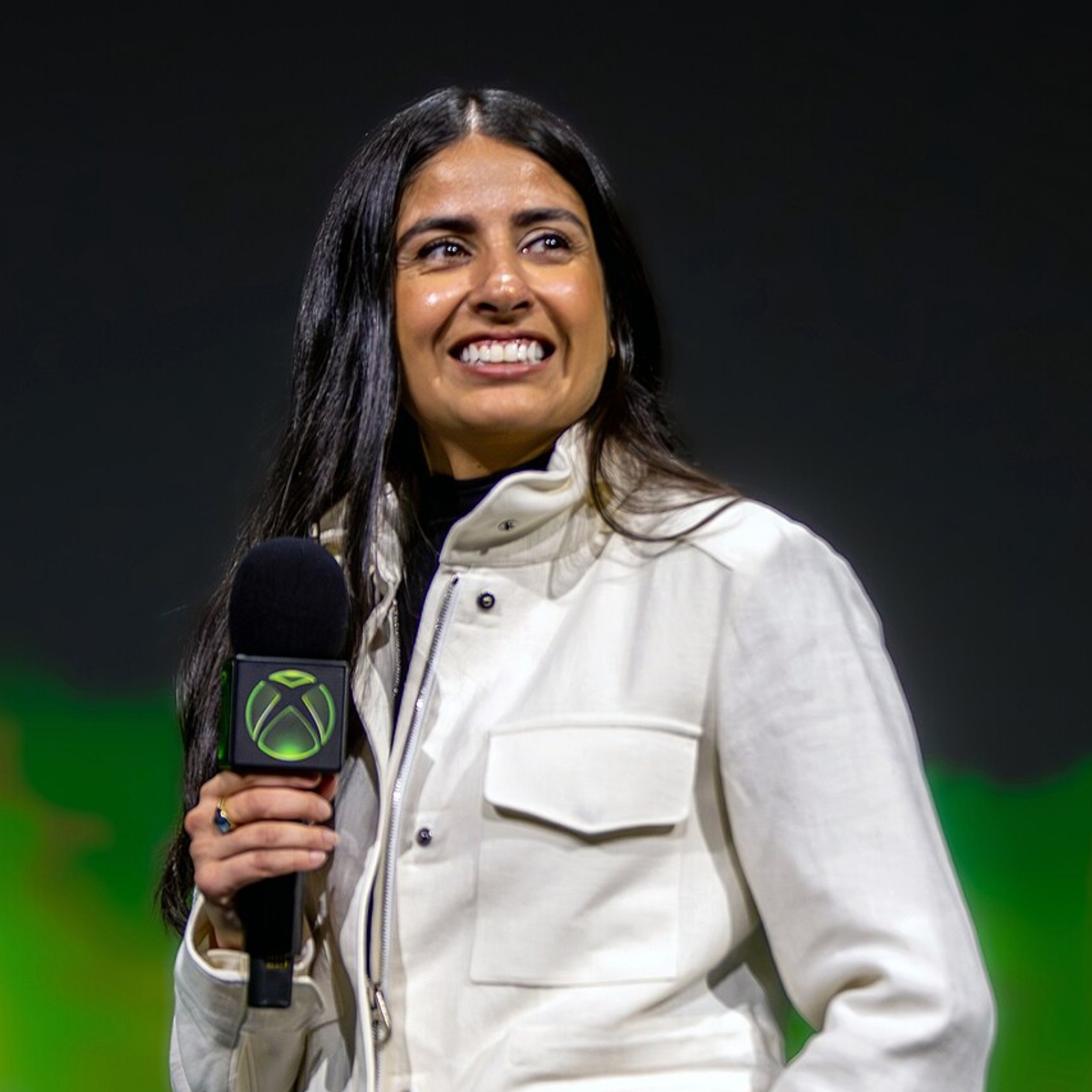 Xbox CEO Asha Sharma smiling on stage holding a microphone
