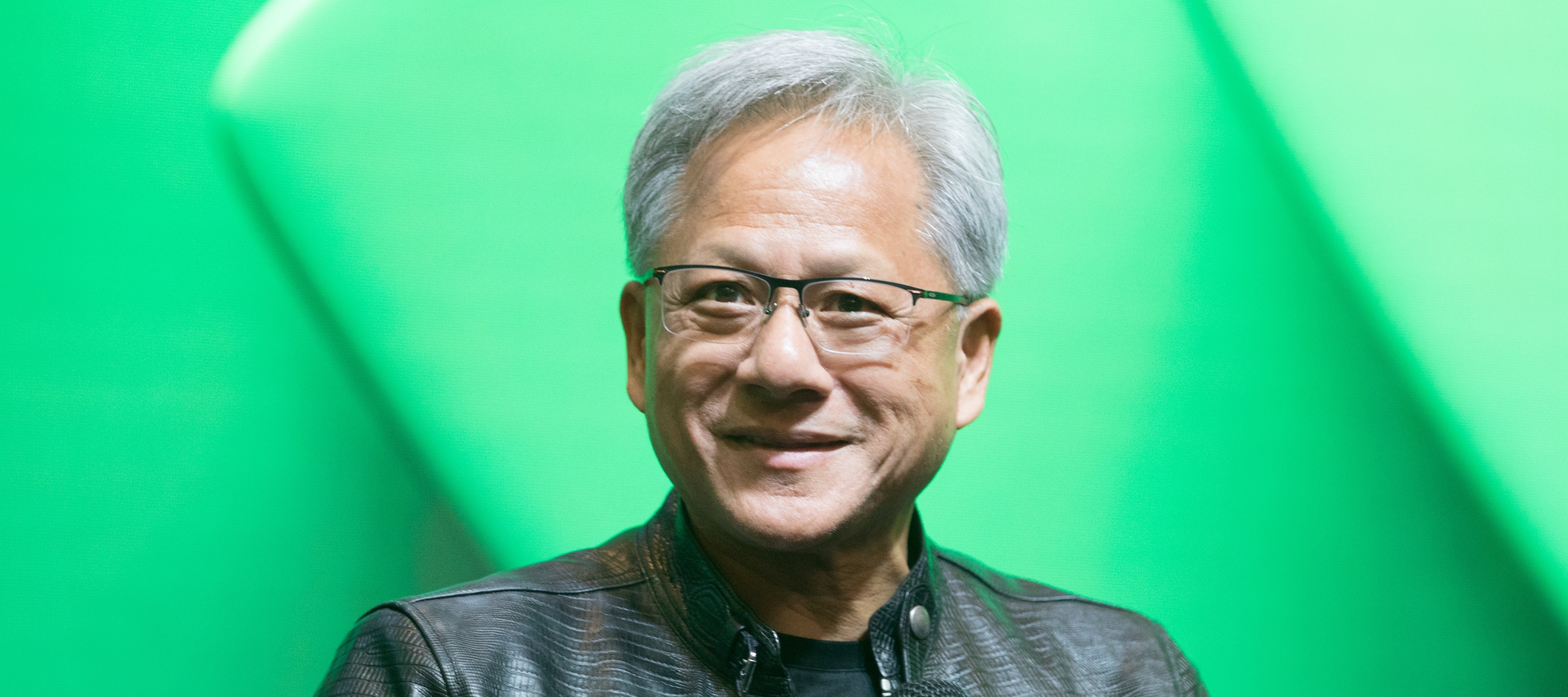 Jensen Huang smiles holding a microphone in front of a green background