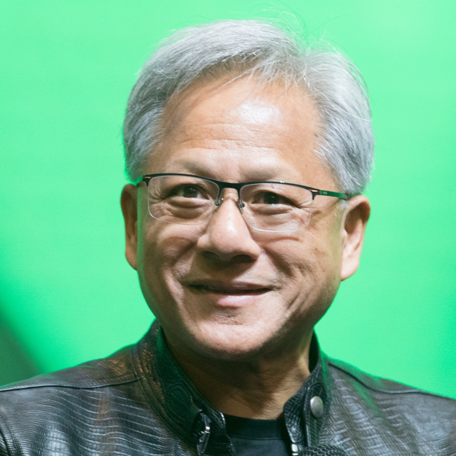 Jensen Huang smiles holding a microphone in front of a green background