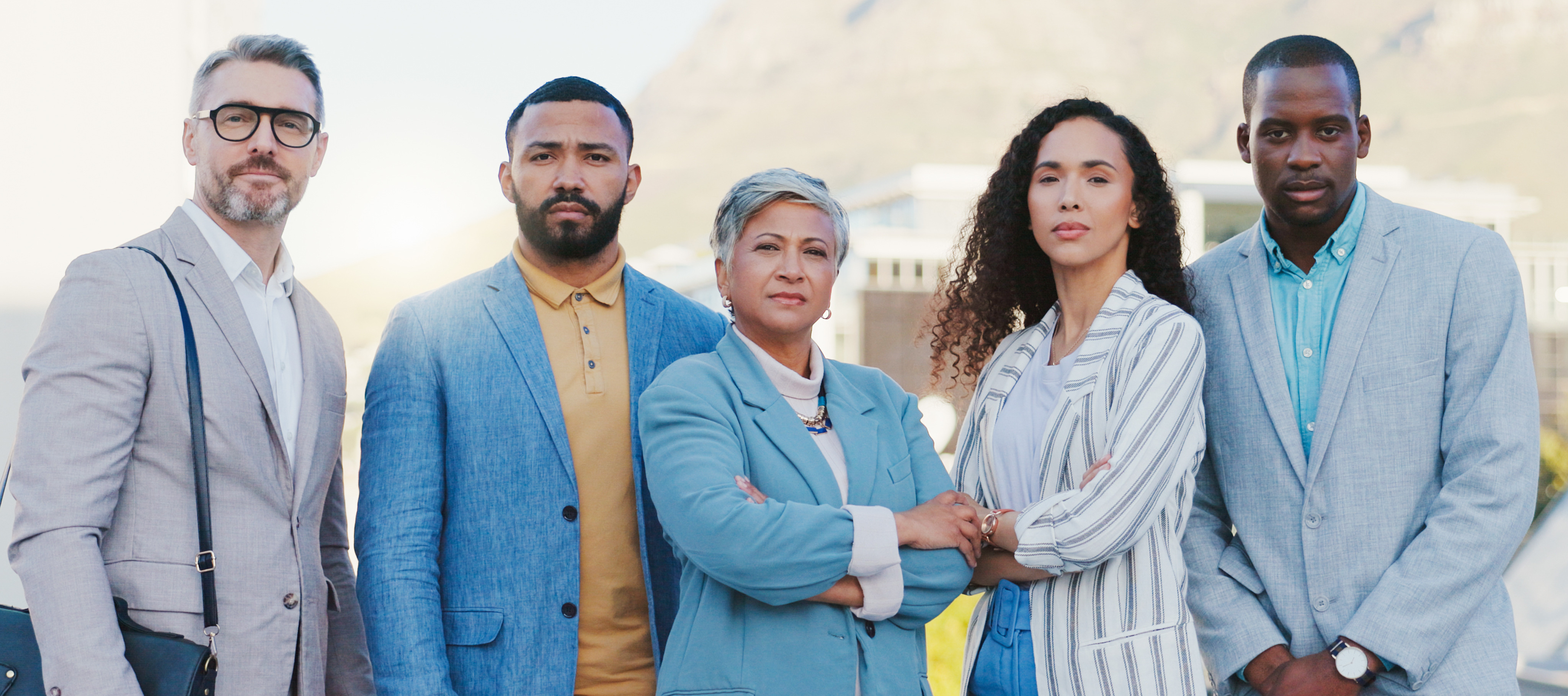 A diverse group of business people stand side by side facing the camera, looking insightful.