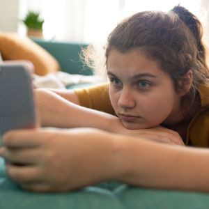 A young girl lays on a couch, holding and staring intensely into a phone screen.