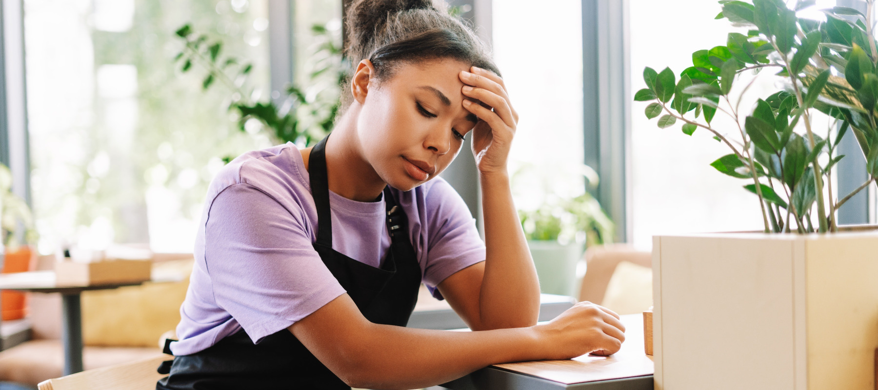 A young woman wearing an apron sitting at a table looking distressed