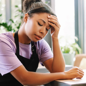 A young woman wearing an apron sitting at a table looking distressed