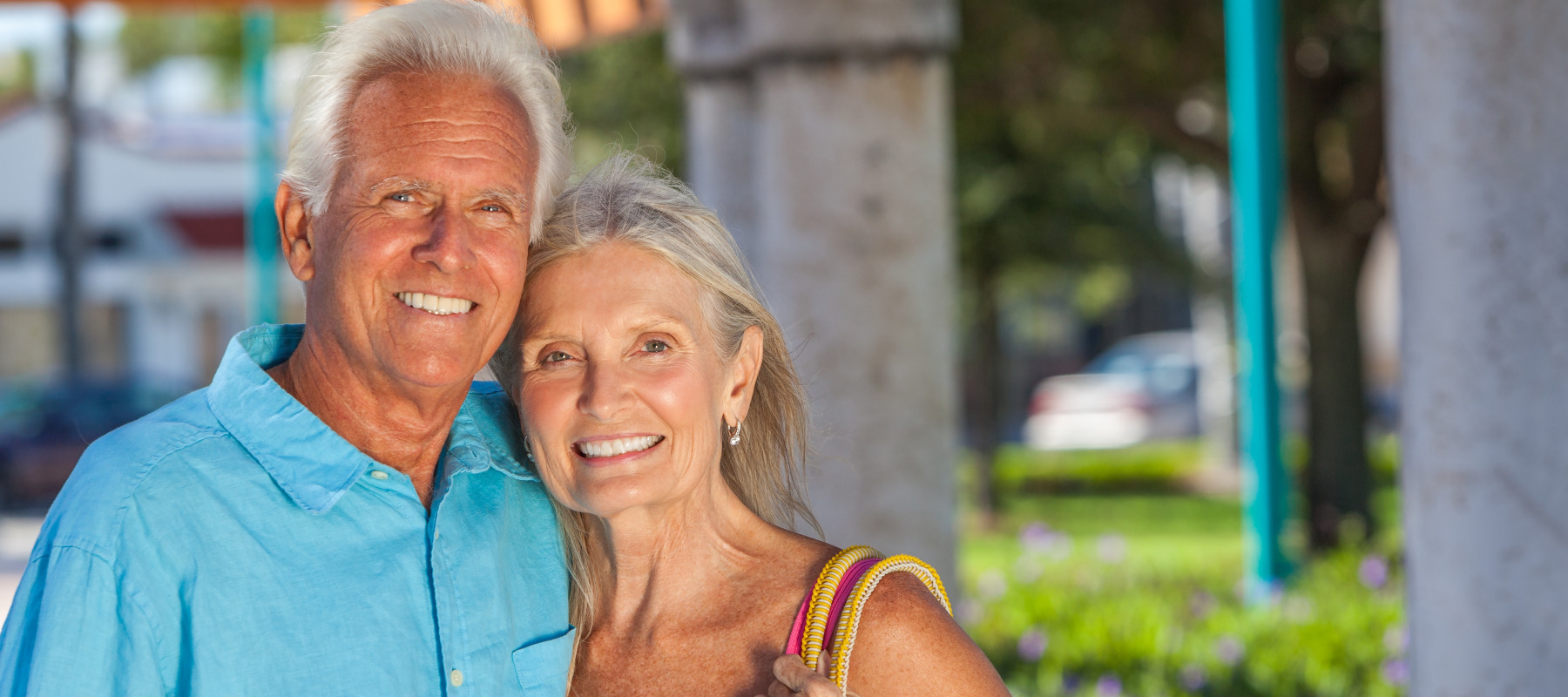 Happy senior man and woman old couple embracing together outside in sunshine.