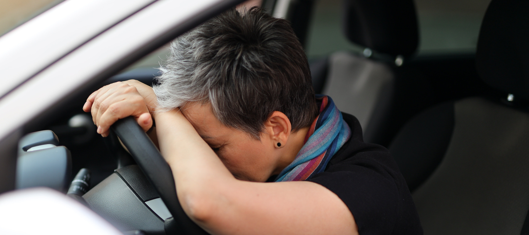 A middle-aged woman with her head on the steering wheel of her car