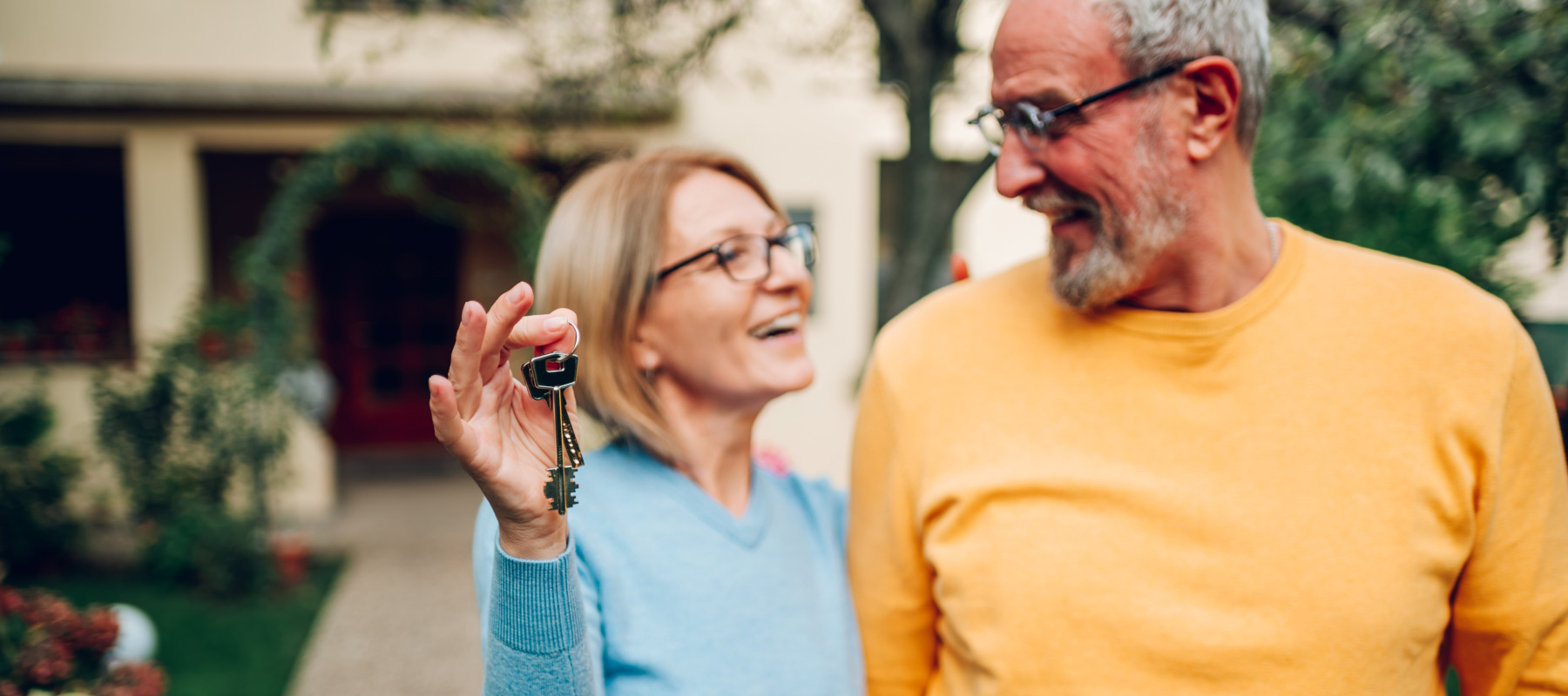 Senior couple holding up new house key while standing out