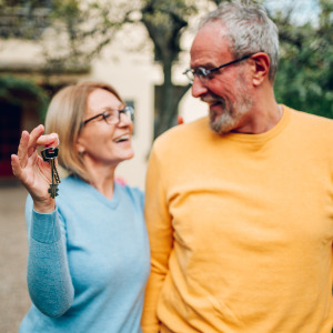 Senior couple holding up new house key while standing out