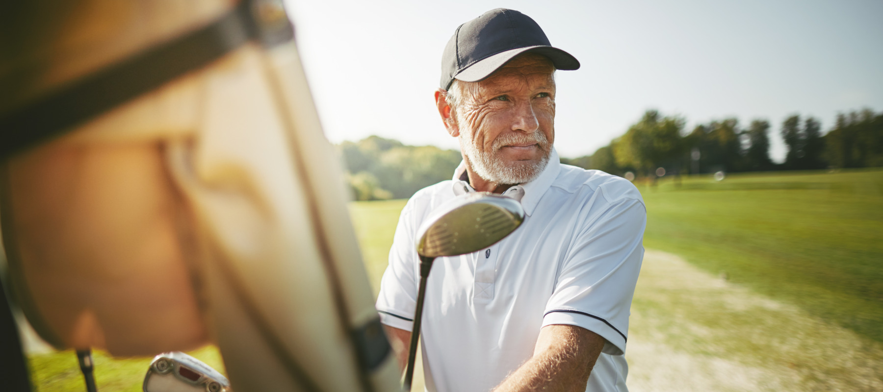 An older man carefully selects a golf club as he prepares to hit the green.