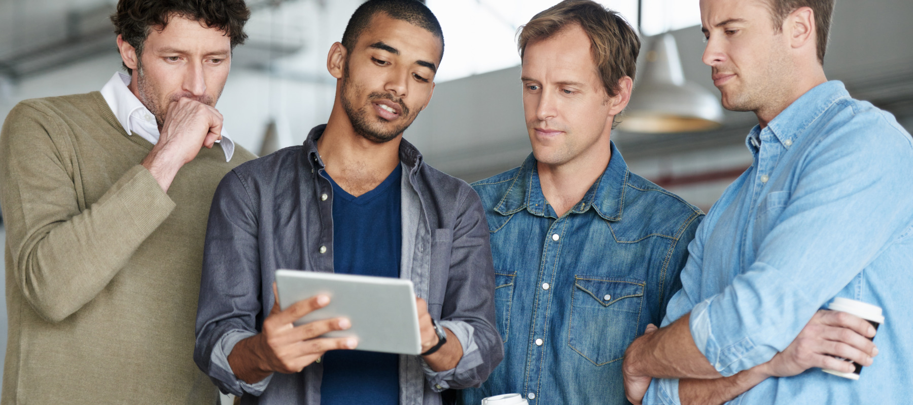 Four adult men with fair and dark curly and straight hair are engaged in a discussion in a modern workspace.