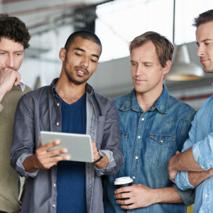 Four adult men with fair and dark curly and straight hair are engaged in a discussion in a modern workspace.
