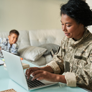 Army veteran woman working on laptop with son playing in the background