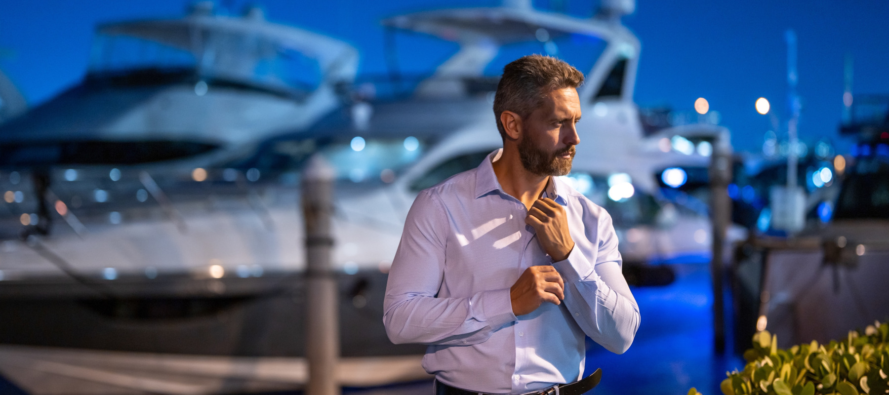 Wealthy charismatic business man at night in front of a yacht.
