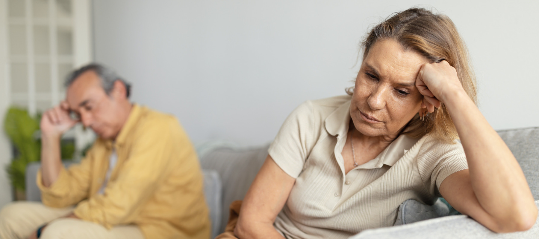 Contemplative couple sits on couch, looking unhappy.