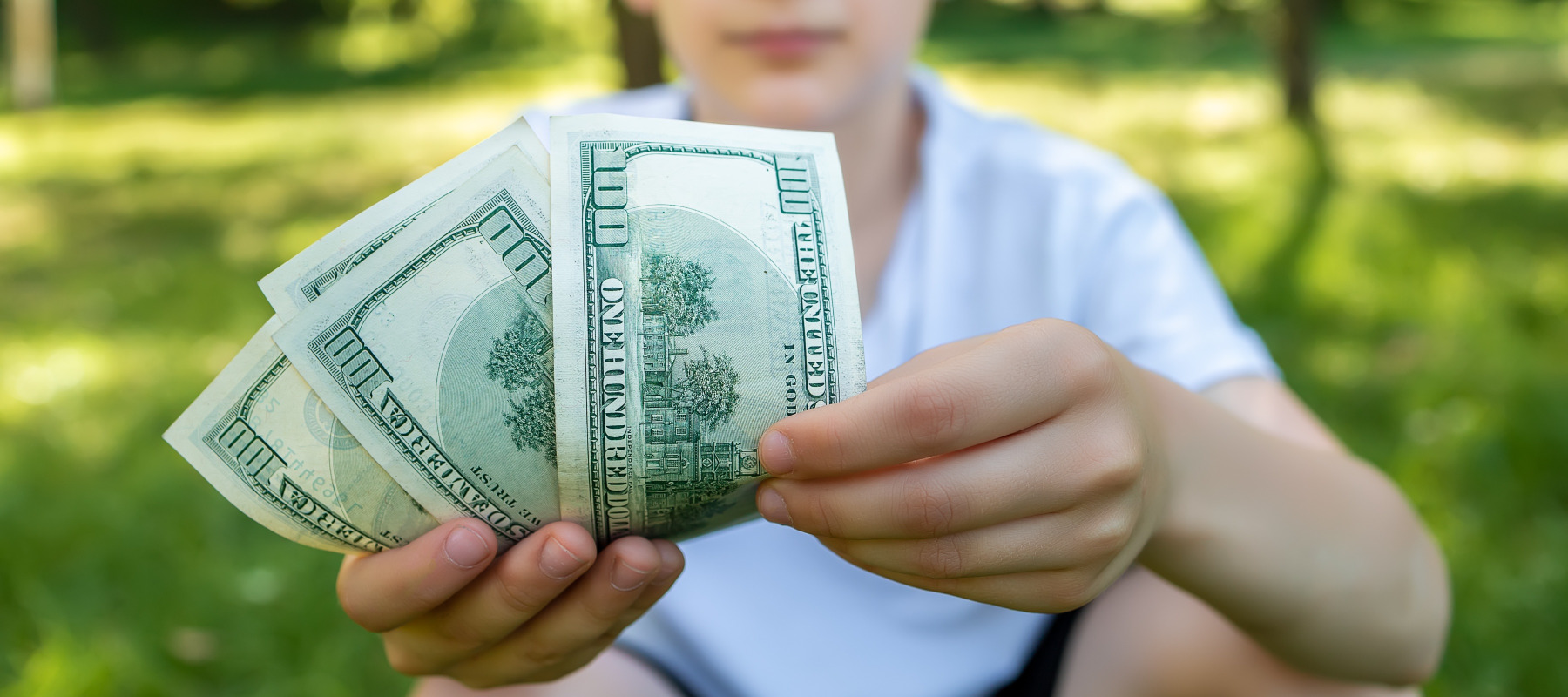 Close up of teenage boy holding $100 bills outside.