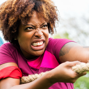 Woman grimaces as she pulls rope in game of tug of war, her teammates seen behind her.