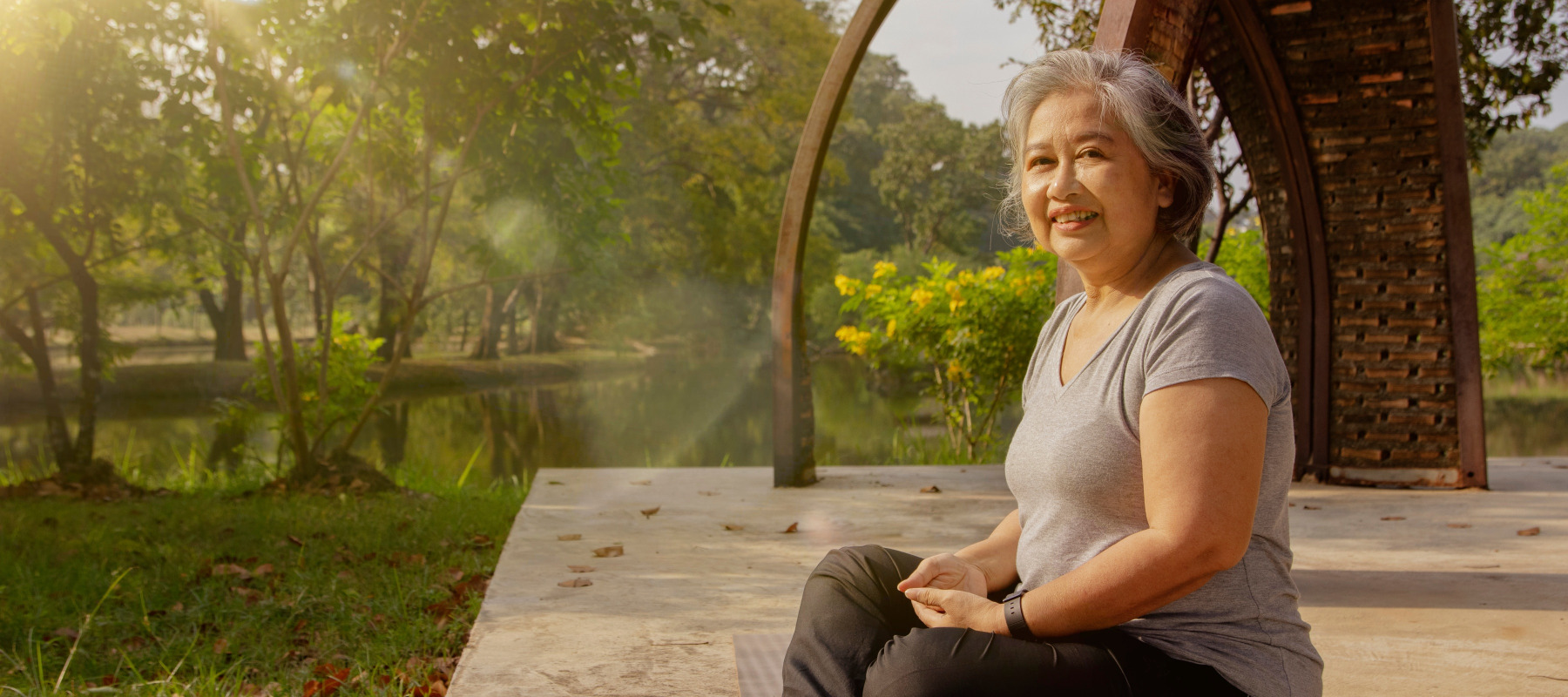 Healthy gray-haired older Asian woman meditates in a park.