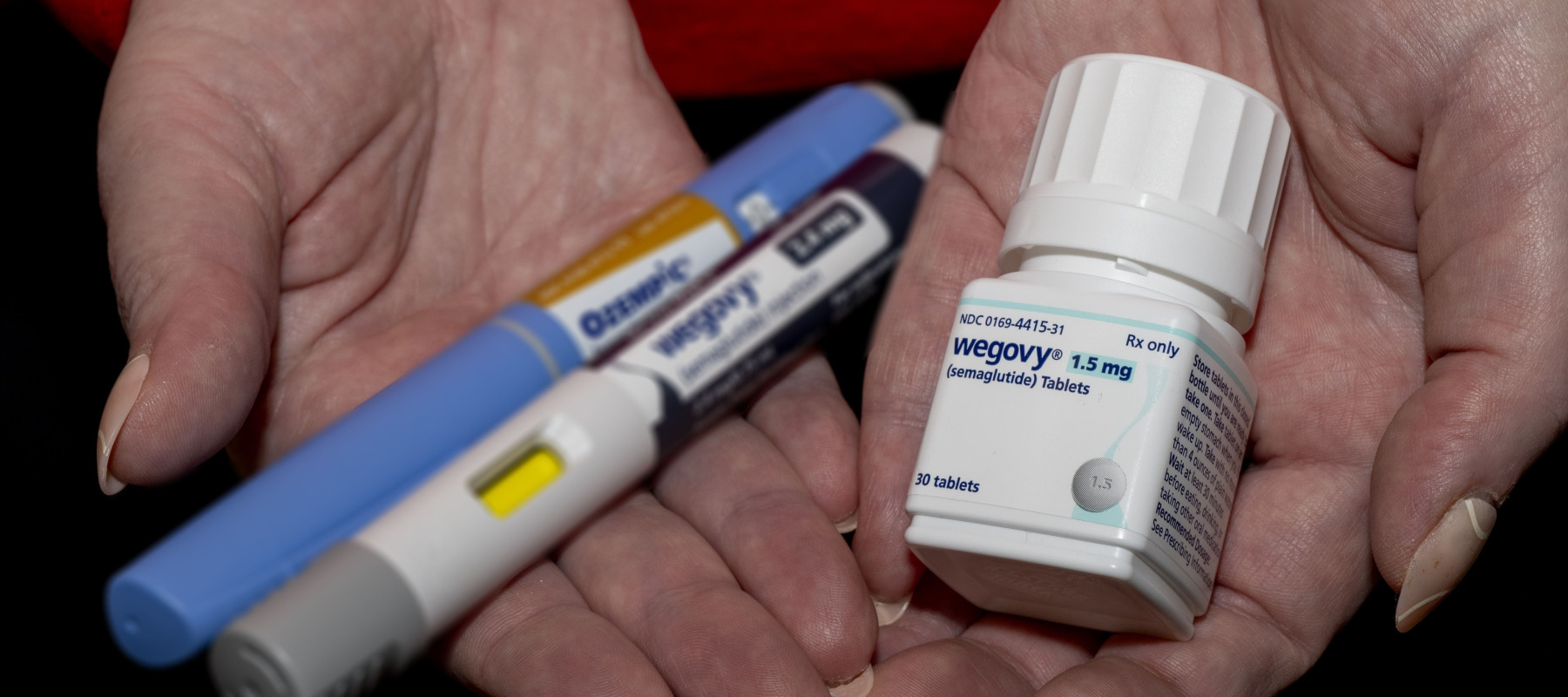 New Wegovy semaglutide tablets with out of focus Ozempic and Wegovy injection pens in a woman's hand.