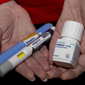 New Wegovy semaglutide tablets with out of focus Ozempic and Wegovy injection pens in a woman's hand.