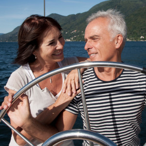 Happy couple look at each other smiling while standing behind the wheel of a sailboat.