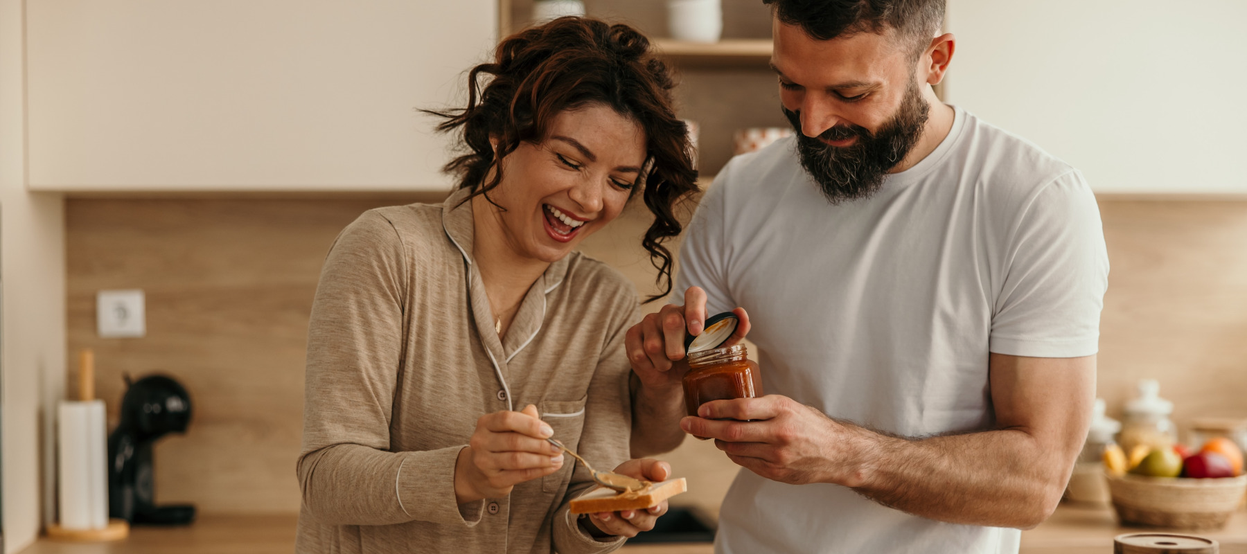 Partners sharing morning meal, spreading jam on toast together.